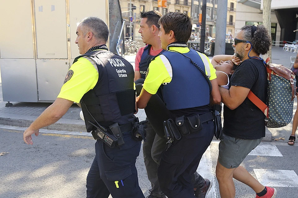 Пострадавшую в теракте в Барселоне несут на руках к карете Скорой помощи.