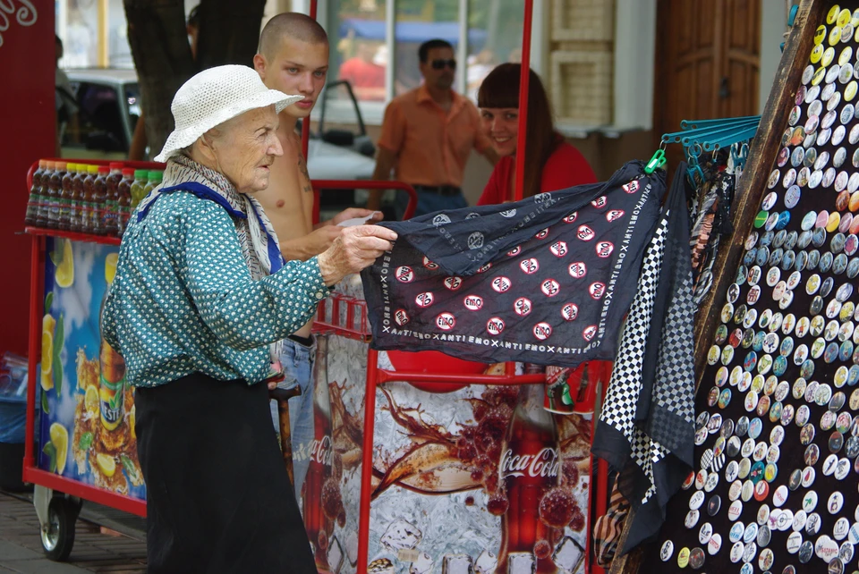 Пенсионерка выбирает модный платок в уличной торговой палатке