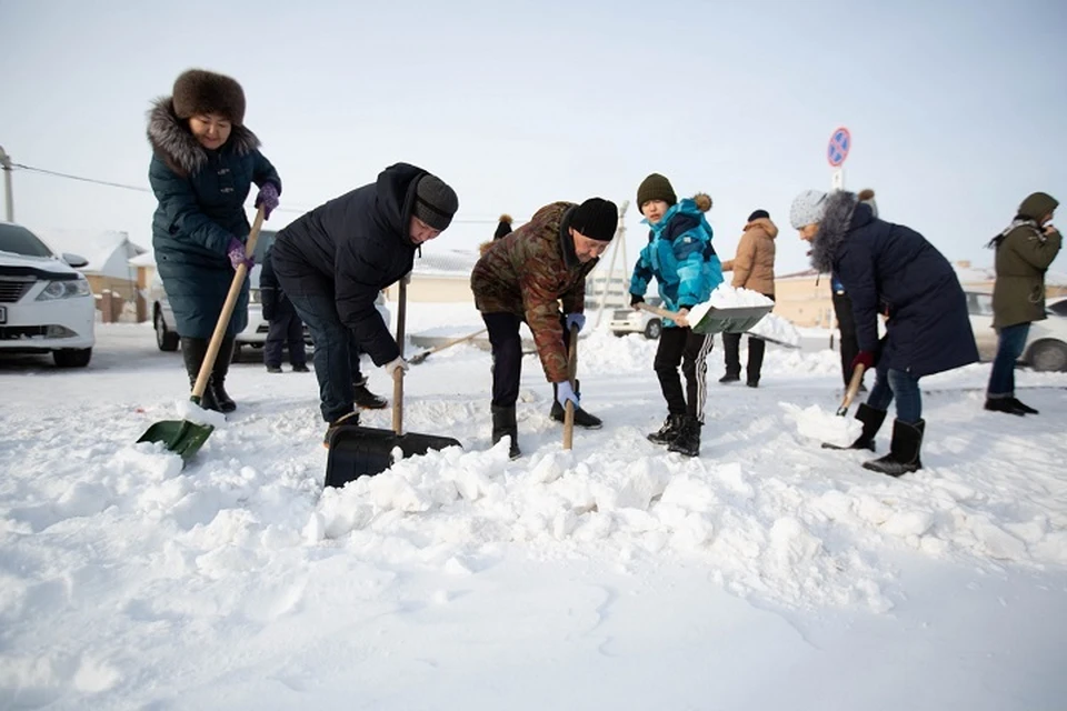 Люди с лопатами в руках помогают коммунальщикам справиться со снежными сугробами.