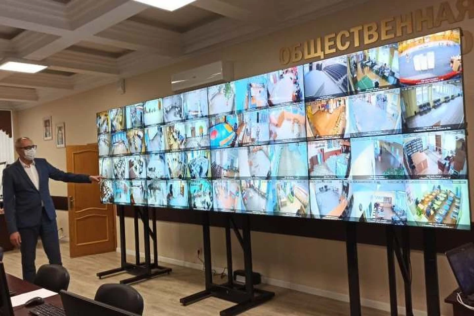 Председатель Общественной палаты Игорь Селиванов показывает стену с экранами, на которых транслируется происходящее на избирательных участках.