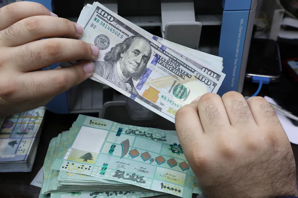 Продавец обмена валюты держит банкноты в долларах США в своем магазине в Бейруте.