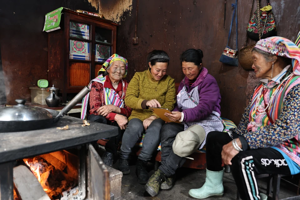 Ли Вэньши (первая слева) и ее дочь Ли Юйхуа (вторая слева) рассматривают фотографии, сделанные десять лет назад, в их доме в деревне Дичжэндан в провинции Юньнань, 6 февраля.