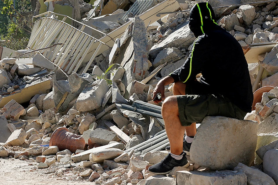 Мужчина сидит на развалинах дома в итальянском городе Аматричи.